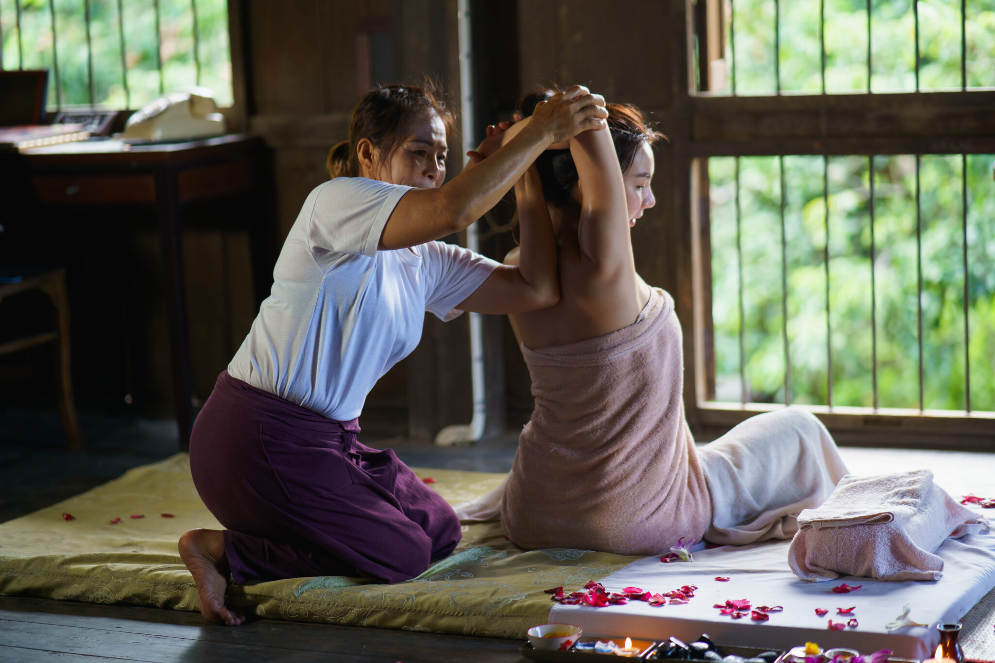Therapist performing an assisted Thai massage stretch with a client wearing comfortable clothing in a peaceful treatment space